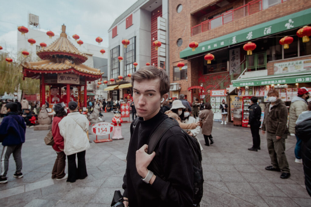 In a busy market in Kobe, Japan, Noah uses headphones to drown out the noise and to reflect on his solo trip. Music is essential for a solo trip. 