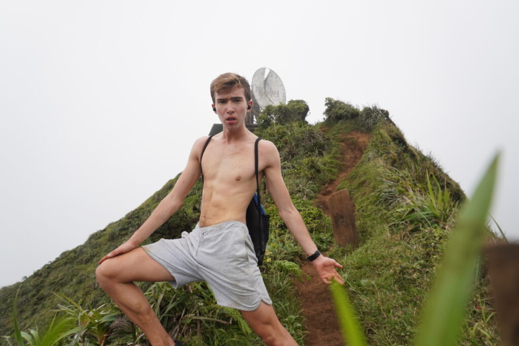 Noah takes a shirtless picture on the  Moanalua Valley Trail with the iconic radio tower from the Haiku Stairs, one of the most famous Oahu hikes.