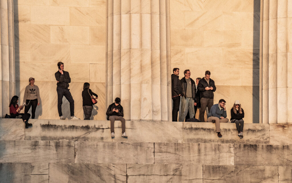 Tourist sit and stand on the steps of the Lincoln Memorial during golden hour. 
