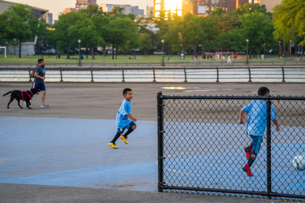 Boys play soccer in Fleshing Meadows Park at golden hour. 